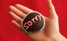 A muffin in the palm of a person's hand with the word "sorry" on it written in frosting