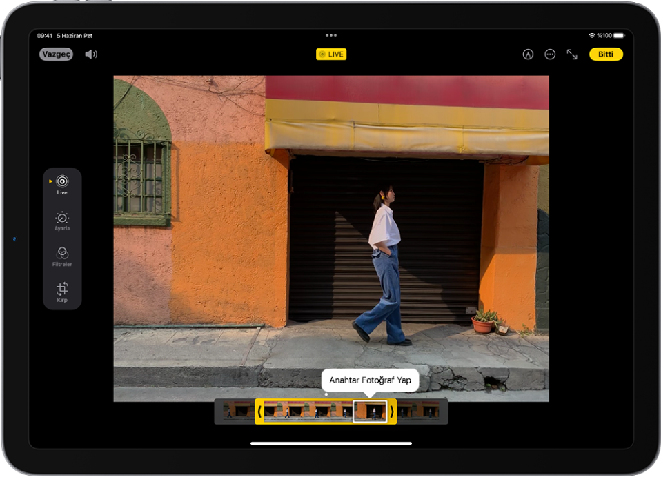 Fotoğraflar uygulamasındaki düzenleme ekranının ortasında bir Live Photo var. Kare görüntüleyici, videonun alt tarafında ve düzenlenen Live Photo’ya dahil edilmek üzere seçilen karelerin çevresinde sarı bir kontur var; anahtar fotoğraf yapmak üzere tek bir kare seçilmiş. Düzenleme araçları ekranın sol tarafında, yukarıdan aşağıya doğru şu şekilde: Live Photo, Ayarla, Filtreler ve Kırp. Live Photo seçili.