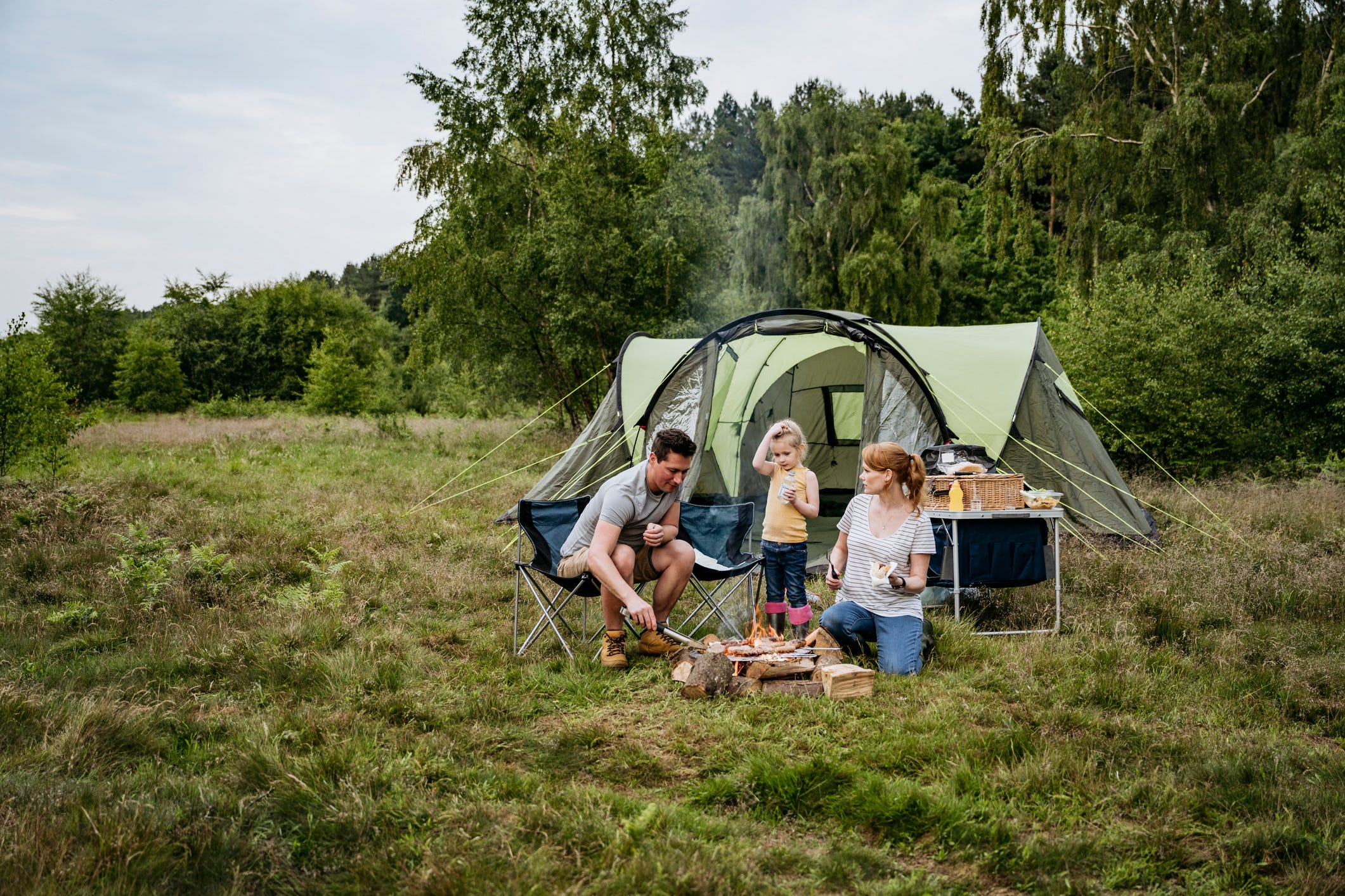 caucasian family with one child enjoying outdoor cooking over open fire on weekend camping trip in late spring