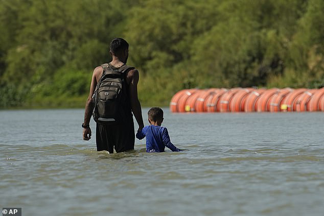 A migrant with a child crosses the Rio Grande river from Mexico into Texas