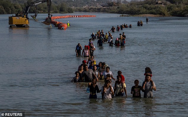 A caravan wades past a string of buoys, being constructed to deter migrants crossings through the Rio Grande river, as they look for an opening in the concertina wire to enter into the U.S.