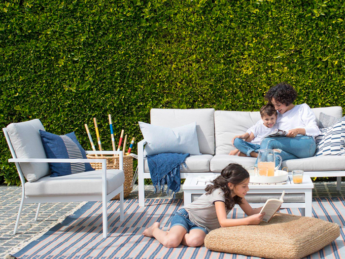 A patio with white yardbird outdoor armchair, sofa, and coffee table and woman and child seated on sofa.
