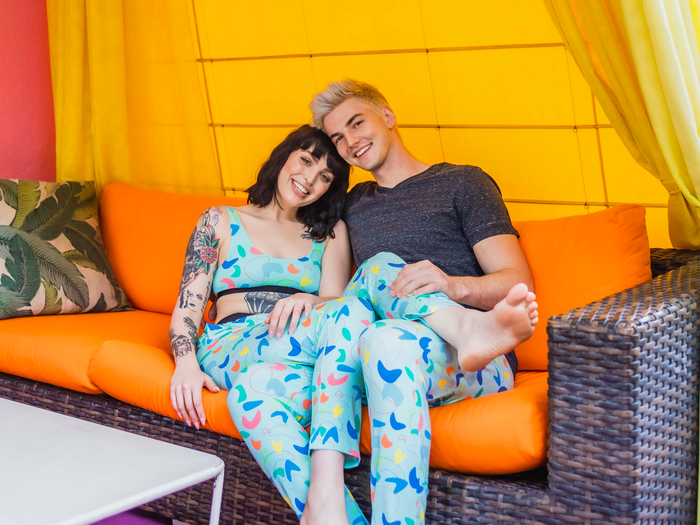 Two people wearing MeUndies blue loungewear with a colorful print and sitting on a couch