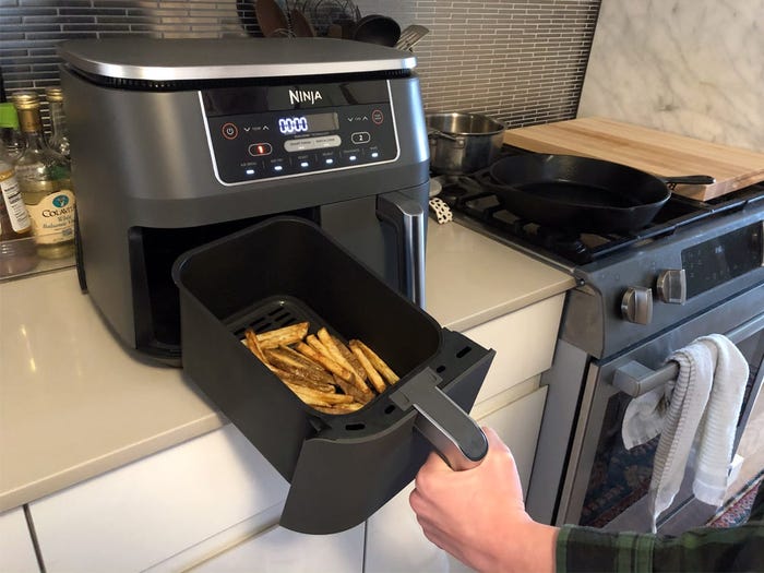 A person pulls a basket containing french fries out of the Ninja Foodi Two-Basket Air Fryer.