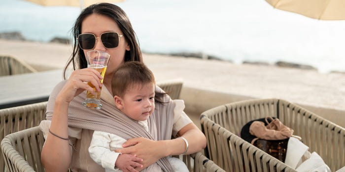 A woman with a toddler sits in a chair while drinking a glass of beer.