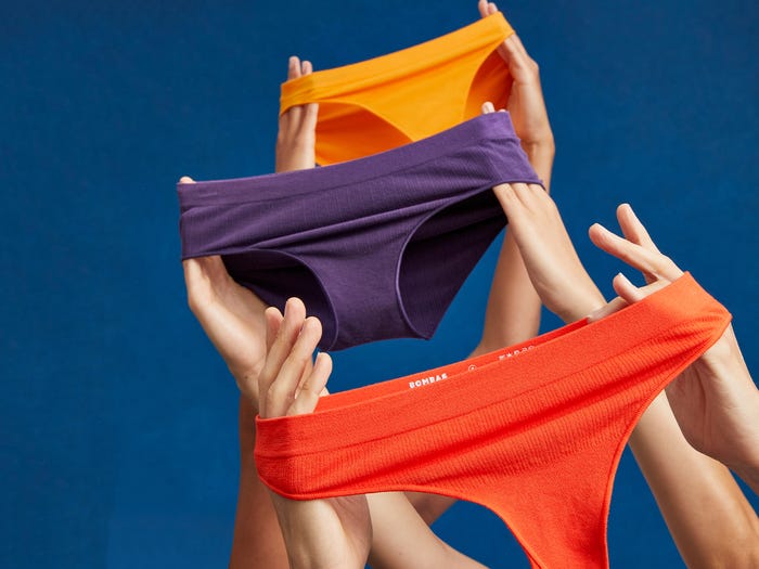Hands holding up three different styles and colors of Bombas underwear.