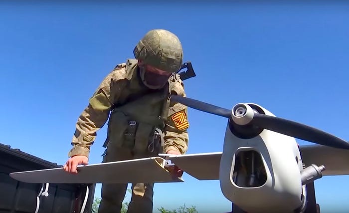 A Russian soldier in combat gear puts a wing on a drone against a blue sky