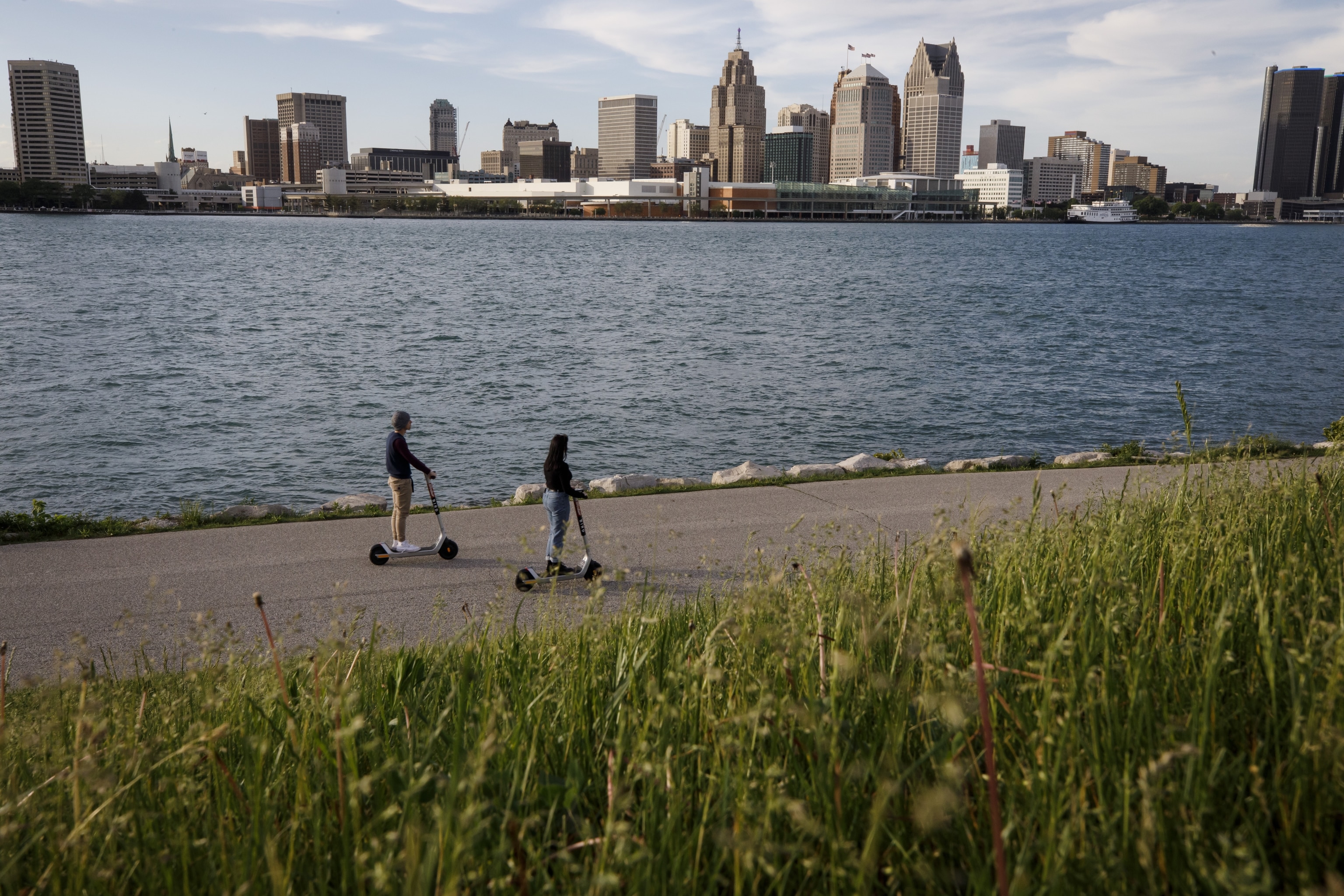 People ride scooters along a waterfront across from Detroit, Michigan, in Windsor, Ontario, Canada