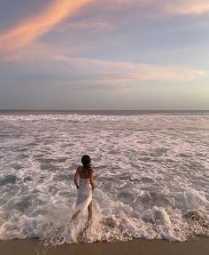 a woman in a white dress walking into the ocean