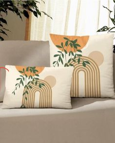 three pillows sitting on top of a couch next to a potted plant