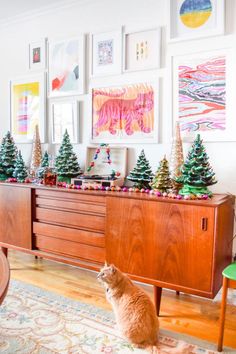 an orange cat sitting on the floor in front of a dresser and christmas tree decorations