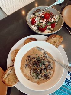 a bowl of mushroom soup next to some bread on a table with other food items
