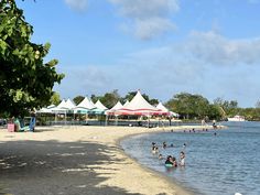 many people are swimming in the water on a sunny day at the beach with white tents