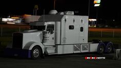 a white semi truck parked in front of a gas station at night with the lights on