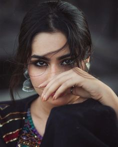 a close up of a person wearing jewelry and holding her hand near her face with both hands