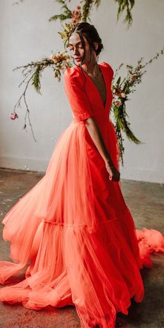 a woman in an orange dress standing next to a floral arrangement and smiling at the camera