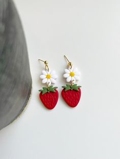 two strawberry shaped earrings with daisies on them sitting next to a planter pot