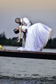 a bride and groom kissing on the end of a dock in front of some water