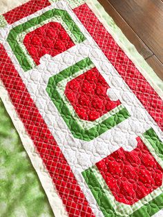 a red and green quilted table runner on top of a wooden floor next to a vase filled with flowers