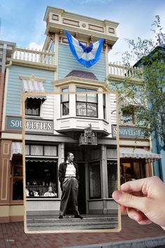 a person holding up an old photo in front of a building with blue and white decorations