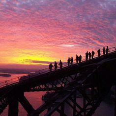 people walking across a bridge at sunset with the sun setting in the sky behind them