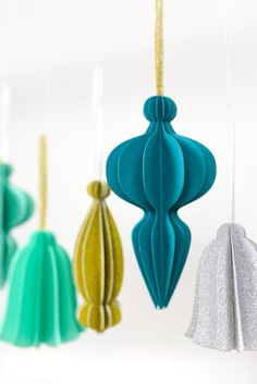 three colorful ornaments hanging from strings on a white background with silver and green decorations in the foreground