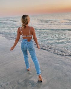a woman walking on the beach at sunset with her back to the camera and arms outstretched