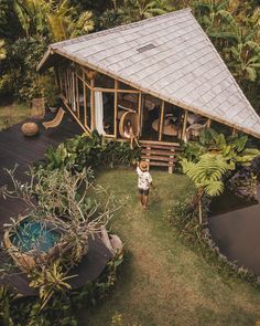 a woman standing in front of a small wooden cabin surrounded by greenery and trees