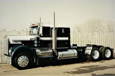 a black and white semi truck parked in front of a fenced off area with snow on the ground