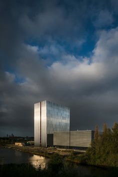 a large building sitting on top of a lush green field next to a river under a cloudy sky