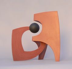 an orange sculpture with a black ball in it's mouth on a white surface