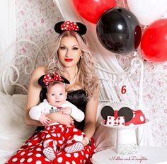 a woman holding a baby wearing minnie mouse ears and sitting on a bed with balloons in the background