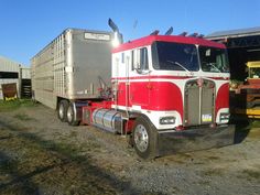 a red and white semi truck parked next to a barn