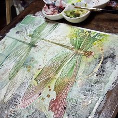a painting with dragonflies on it sitting on a table next to bowls and spoons
