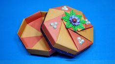 an origami box with a flower and pearls on the lid sitting on a blue surface