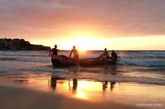 three people in small boats on the beach at sunset