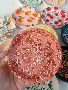 a hand holding a plate with flowers painted on it and other plates in the background