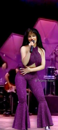 an image of a woman in purple outfit singing into a microphone at a concert or show