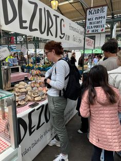 a woman standing in front of a counter filled with donuts and other food items