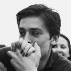 a black and white photo of a man holding his hands to his mouth with people in the background