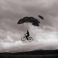 a man riding a bike under umbrellas in the air with an overcast sky behind him