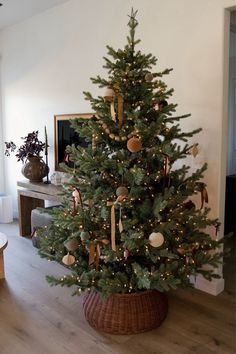 a small christmas tree in a basket with ornaments on the top and lights around it