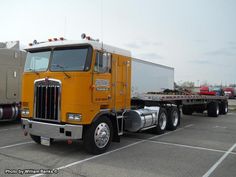 a large yellow semi truck parked in a parking lot next to other trucks and trailers