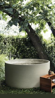 an outdoor bathtub sitting under a tree in the middle of some grass and bushes
