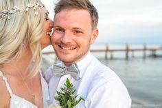 a bride and groom are posing for a photo by the water with their heads together