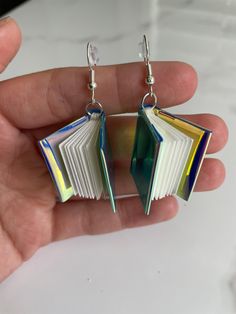 a pair of earrings that are shaped like an open book with colorful pages hanging from them