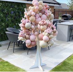 a tree made out of balloons in a backyard with an outdoor dining area behind it