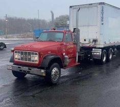 a red semi truck driving down a wet road in the snow with other trucks behind it