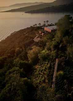 an aerial view of a house on top of a hill near the ocean at sunset