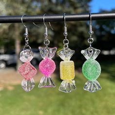 three different colored glass earrings hanging from a hook on a pole in front of some grass